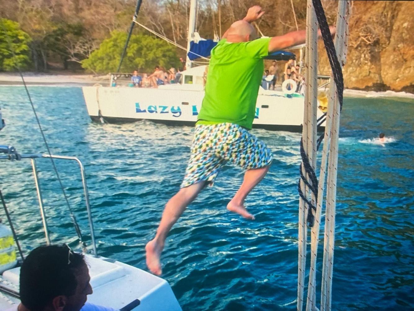 Person in green shirt jumping off boat into water near another boat.