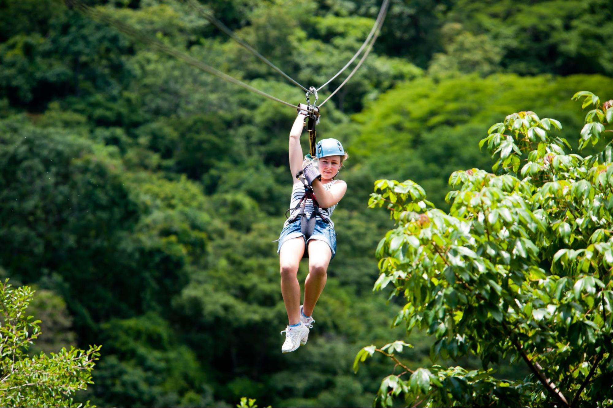 Person ziplining through a forest with lush green trees in the background.