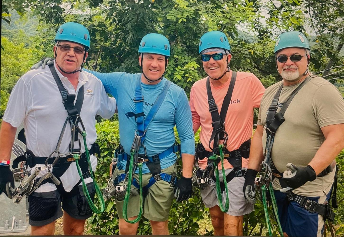 Four men in helmets and harnesses smiling in a forest setting.